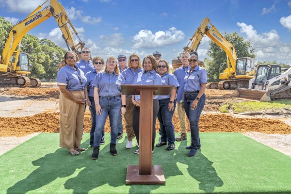 Lineup of eleven people at the groundbreaking ceremony for Bayside Breeze. Podium in front of the people. Construction equipment in the background.