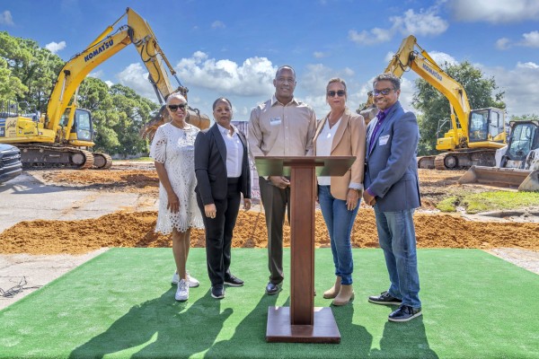 Lineup of five people at the groundbreaking ceremony for Bayside Breeze. Podium in front of the people. Construction equipment in the background.