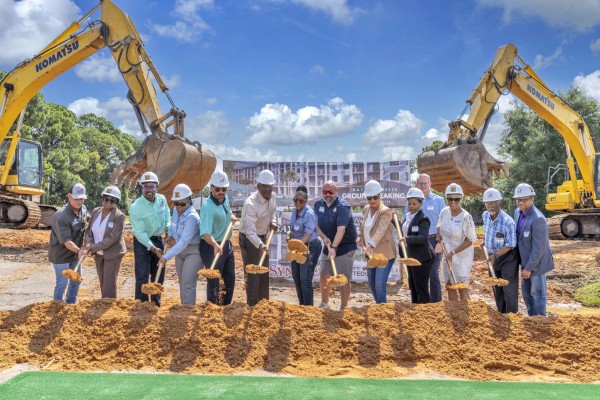 Lineup of people holding shovels full of dirt at the groundbreaking ceremony for Bayside Breeze. Large pile of dirt front of the people. Construction equipment in the background.