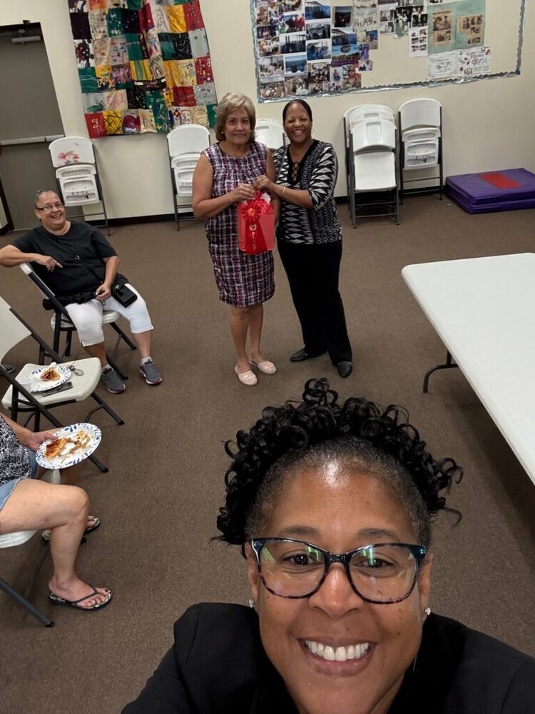 A woman taking a selfie in the foreground with two women smiling in the background.
