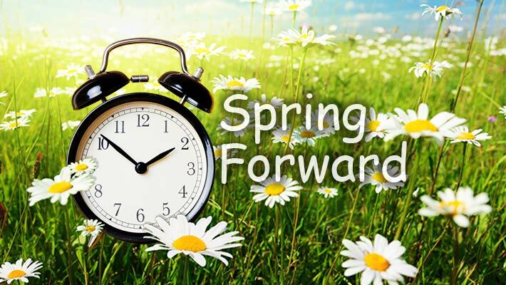 Spring forward. Alarm clock in a field of flowers.