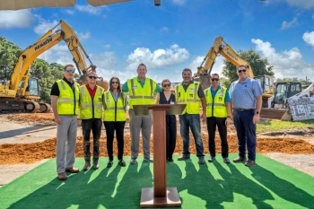 Lineup of eight people at the groundbreaking ceremony for Bayside Breeze. Podium in front of the people. Construction equipment in the background.