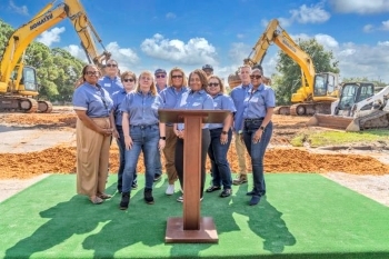 Lineup of eleven people at the groundbreaking ceremony for Bayside Breeze. Podium in front of the people. Construction equipment in the background.