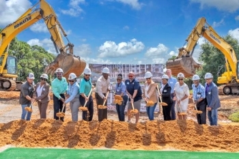 Lineup of people holding shovels full of dirt at the groundbreaking ceremony for Bayside Breeze. Large pile of dirt front of the people. Construction equipment in the background.